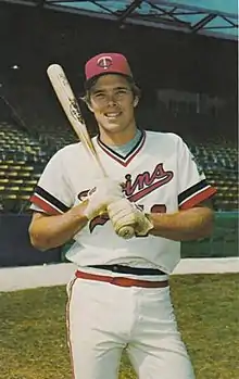 A man wearing a white baseball uniform holding a baseball bat in two hands