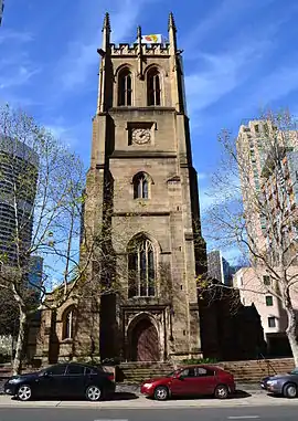 view looking up at a tower with paired windows in the upper level, crocketted pinnacles and decorated battlements