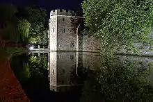 Night scene of floodlight stone walls adjoining still water.