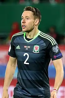 A footballer with dark hair wearing a black tracksuit