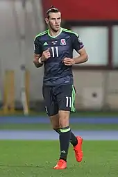 A footballer wearing a dark T-shirt and dark shorts.