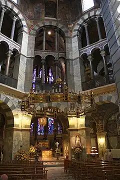 The interior of a tall octagonal church, rising in three rows of decorated arches. A large candelabra hangs above the central altar.