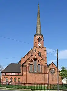 a red brick building with tiled roof and needle spire.