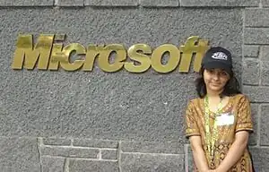 Photograph of Arfa Karim standing next to a golden Microsoft company logo on the wall of Microsoft's headquarters in Redmond, Washington, United States