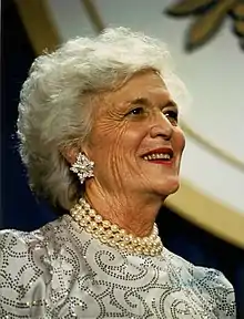 Barbara Bush, wearing pearls and a dress, is shown smiling