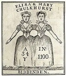 Two women, apparently joined at the shoulder. The women are wearing a single skirt between them. The women's facial features and hair colours are not identical.