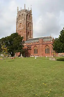 Red stone building with square tower. In the foreground is a graveyard.