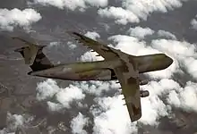 Four-engined jet transport with dark green and gray paint scheme in-flight above clouds