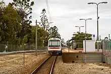 A train stopped at a station platform viewed from a pedestrian level crossing behind