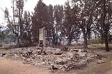 The foundation of a house covered in burnt debris. A chimney is still standing.