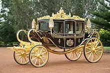 A very ornate coach, black with gold trim, a coat of arms on the door