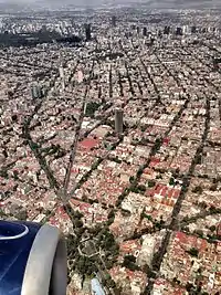 Aerial view of Colonia Del Valle. At bottom, the park at the junction of Division Del Norte, Eje 3 Poniente Amores, San Antonio and Ave. Colonia Del Valle. In background, Condesa (left) and Roma (right) districts and the Paseo de la Reforma skyline. In the middle, the Torre AXA México, formerly Mexicana Tower.