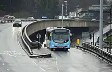 View of the anticlockwise carriageway and the entry slip road on a wet day, with a bus about to join the ring road