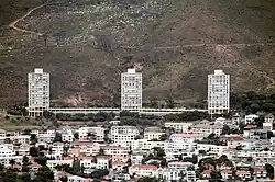 Three large, cylindrical towers tower above a suburb at the base of a mountain.