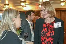 Fiona Davis, a woman wearing a blazer and a red top, smiling at a patron of a book fair.