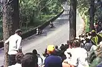 TT race spectators at the exit to Glen Helen in 1969 with two travelling marshals passing by towards Creg Willey's Hill