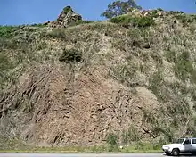 Photograph of a rock formation with a road and a car at its bottom.