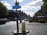 A church building on the left and shopping centre on the right. In the middle a busy road.