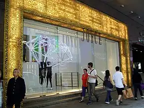 Glass shopfront with textured, illuminated border, from which a sign saying "Joyce" hangs.