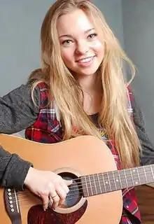 A blond woman holding a guitar