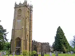 Stone building with arched windows and square tower. In the foreground are gravestones.