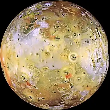 A multi-colored image of the full disk of a planetary body, dotted with numerous dark spots. Much of the middle portion of the planetary body is yellow to white/gray, while the polar regions at the top and bottom are generally reddish in color.