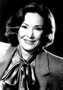 Black and white photo of a smiling woman about fifty years of age and wearing a jacket and tied-up scarf