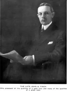 A man with glasses and a comb-over haircut looks into the camera, holding a newspaper. caption reads, "THE LATE JOHN A. FINCH, who possessed all the qualities of a good man, and many of the qualities of a great man."