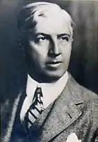 Bust of white-haired man wearing suit and tie