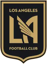 A black shield logo with a gold outline. The shield is flat on the top and sides, and curves to a centered point at the bottom. In the middle is a large gold "LA" in a bold art deco font, with the crossbar of the letter A replaced with a prominent angelic wing made of four lines, angled up and to the left, each line a bit longer than the one below it to create the wing shape. Above and below the "LA" text, it reads "LOS ANGELES" and "FOOTBALL CLUB" respectively in small print (using the same gold color and art deco font).