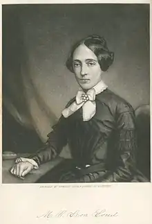 Waist-length portrait of the writer, seated at a table, with a book.