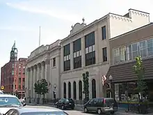 A city street with parked vehicles on either side in front of a series of stone buildings