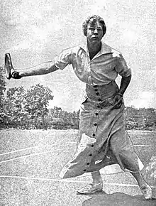 A white woman playing tennis, wearing a long buttoned skirt and a short-sleeved blouse.