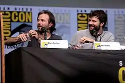 Matt Duffer on the left, with Ross Duffer on the right, both seated behind a table with name cards in front of them and looking to the viewer's left, with a San Diego Comic-Con BBanner in the background