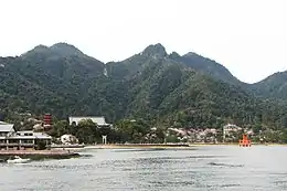 Sea and wooded hills. There is a red pagoda on land and a red gate standing in the water.