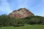 Rocky mountain colored red among green landscape.