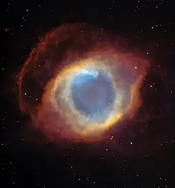 Colorful shell which has an almost eye like appearance. The center shows the small central star with a blue circular area that could represent the iris. This is surrounded by an iris like area of concentric orange bands. This is surrounded by an eyelid shaped red area before the edge where plain space is shown. Background stars dot the whole image.