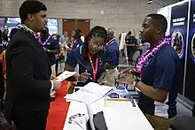 3 people speaking, two wearing blue shirts and one in a suit.