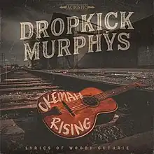 A guitar with "Okemah Rising" written on it in white lying on a train track