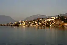 A collection of houses and other small buildings scatter the shore of a wide lake