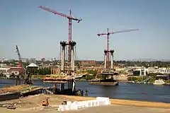 A cable-stayed bridge with the deck partially built and a construction crane atop each of the two pylons