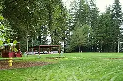 Photograph of a grassy field surrounded by tall evergreen trees, with two reviewing stands at the side.