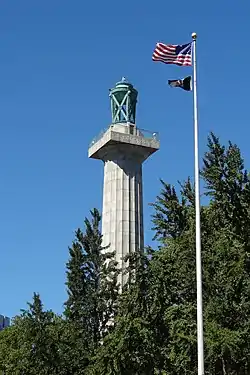 The column of the Prison Ship Martyrs' Monument, topped by a bronze urn, among trees, with a modern American and POW/MIA flagstaff adjoining.