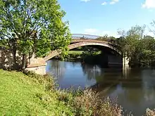 A cast iron bridge over a river surrounded by fields and trees