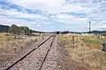 Looking east along the railway line from level crossing on Bylong Valley Way near Sandy Hollow, showing rear end of train waiting on crossing loop