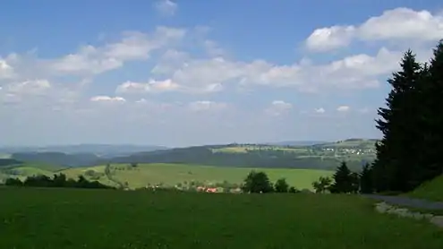 View from the Eckartsberg of Schnett and the Simmersberg (781 m, right) with its subpeak, the Kohlberg (718 m, centre). Between them in the background can be seen the Adlersberg (849,9 m) with the Neuhäuser Hügel (891 m). Left of the Kohlberg in the background is the trading estate of Suhl-Friedberg and the Little Thuringian Forest  with the Schleusinger Berg (671 m) and Schneeberg (692 m). Front centre is the village of Waffenrod/Hinterrod.