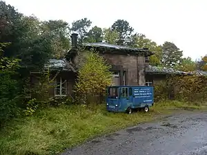 Dilapidated stone building surrounded by overgrown foliage and an old panel delivery van in front