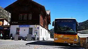 Two-story building with gabled roof; a bus is parked next to it