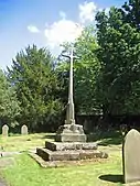 A stone cross base and part of the shaft, set on steps and surmounted with modern wooden cross