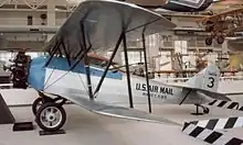 A blue-and-white biplane with "U.S. Air Mail" on the fuselage and "3" on the tail